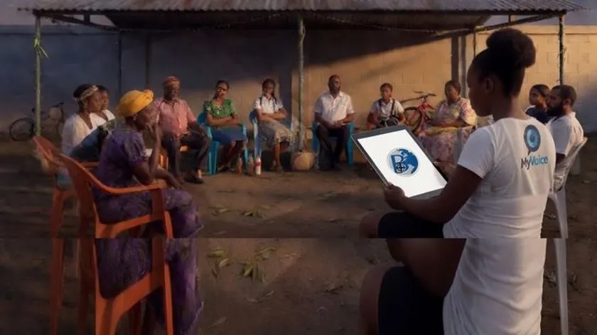 A myVoice interviewer with a tablet talking with a community group in Jamaica
